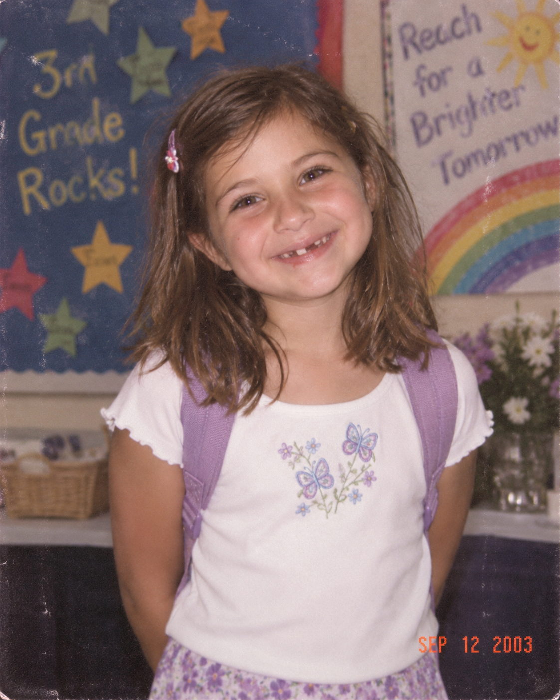 A young girl at a school desk in front of a hand-painted classroom sign