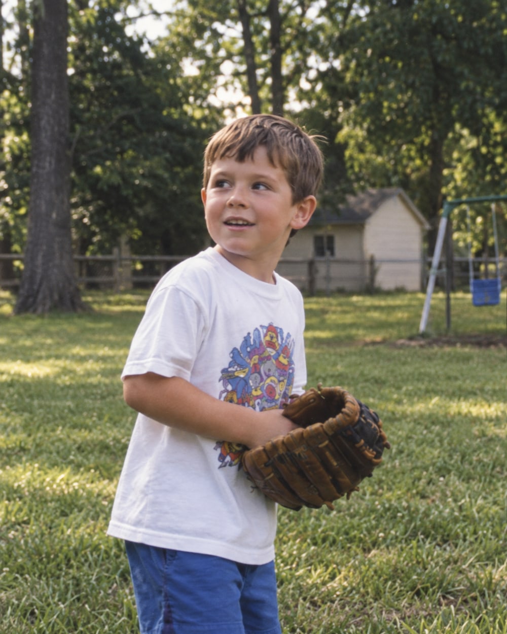 A boy in a baseball shirt holding a glove on a lawn